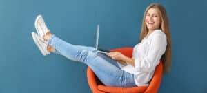 Bild von einer jungen Frau, die mit ihrem Laptop auf einem Sessel sitzt